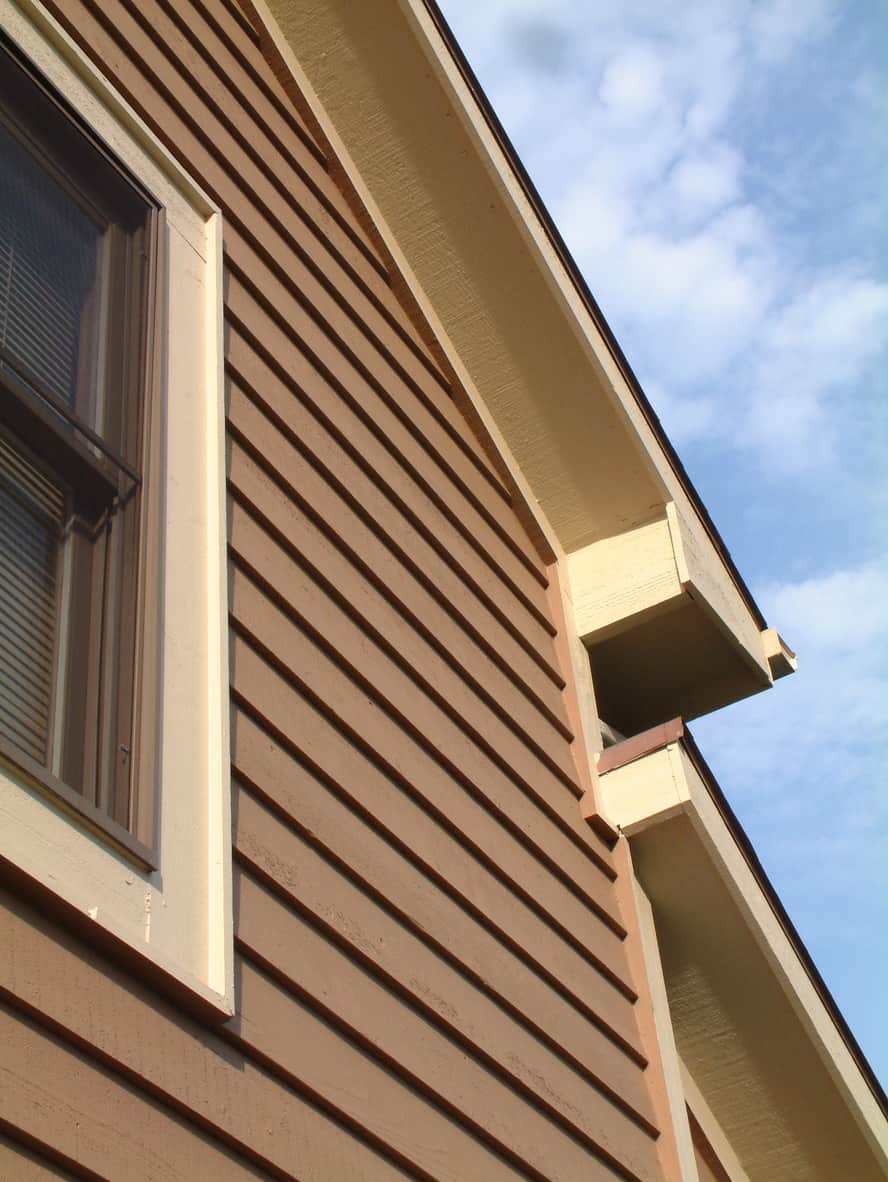 House window with cedar wood siding, roof line, blue sky and clouds.