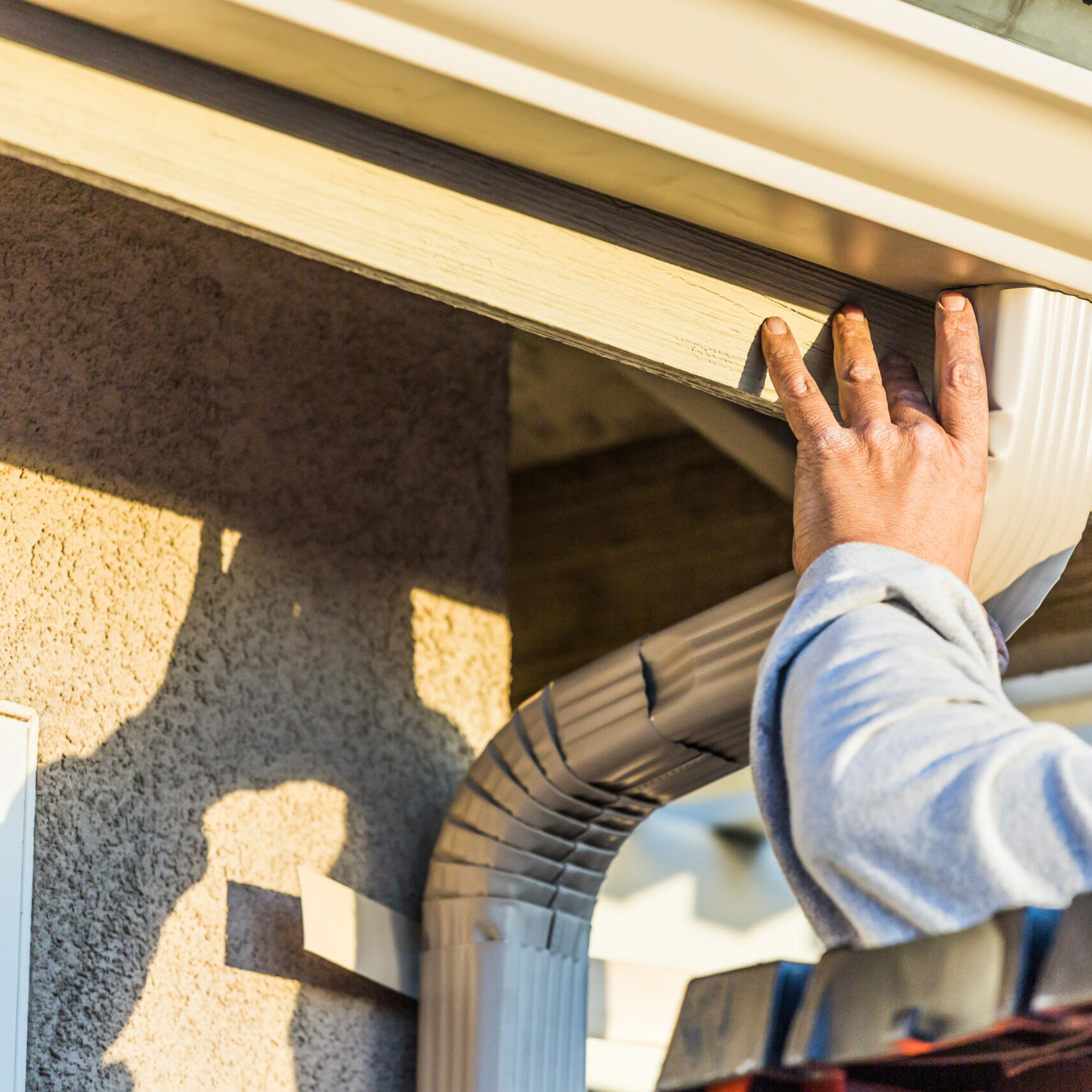 Worker Attaching Aluminum Rain Gutter and Down Spout to Fascia of House.